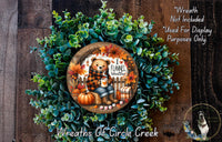 A wreath made of green leaves and a wooden frame, featuring a teddy bear and autumn-themed decorations.