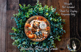 A wreath made of green leaves and a wooden frame, featuring a teddy bear and autumn-themed decorations.