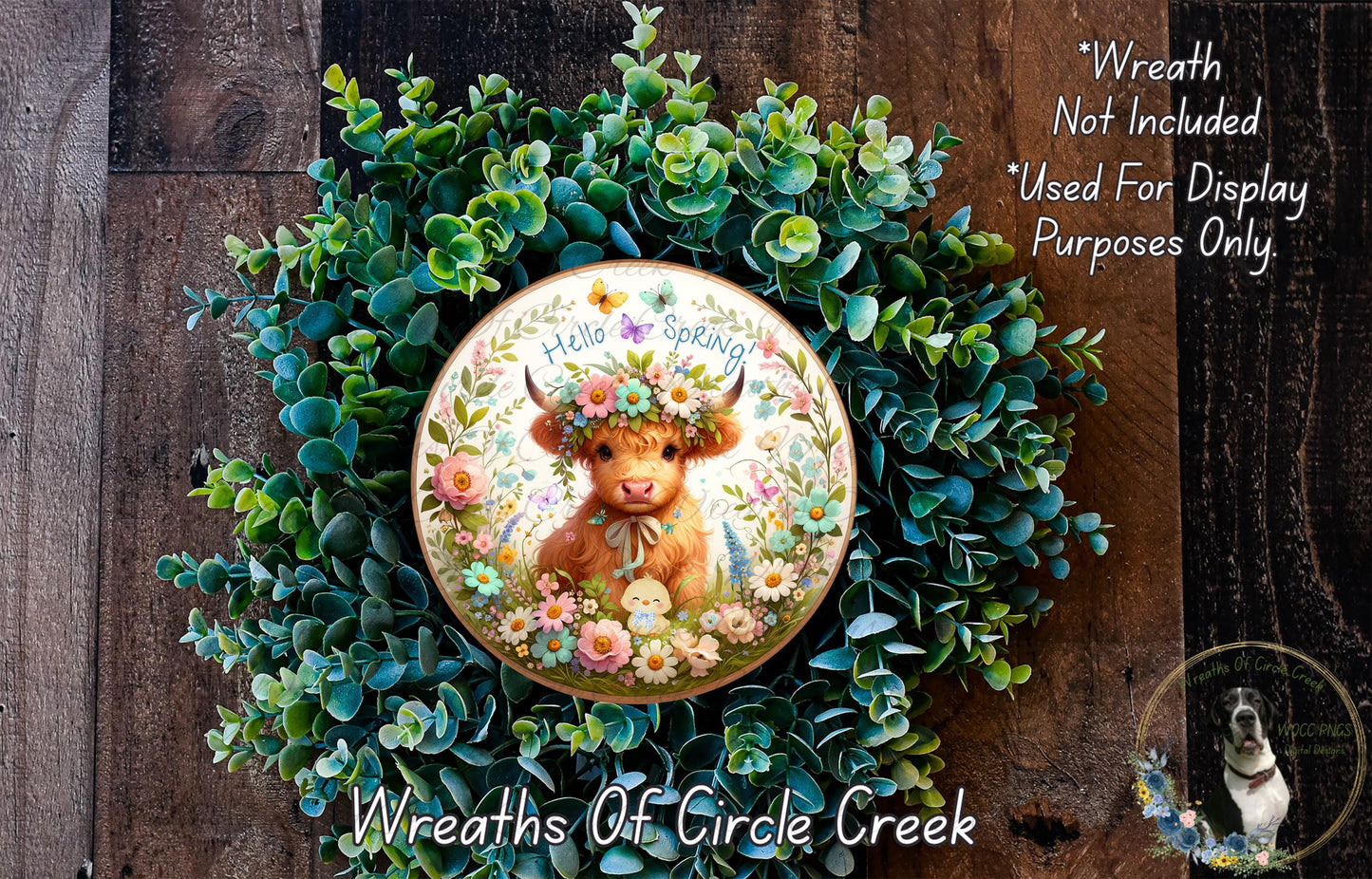 A wreath made of green leaves and flowers, with a cow wearing a flower crown in the center. The wreath is displayed on a wooden surface.