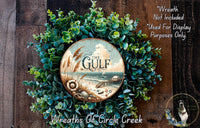 a wreath made of green foliage and a circular wooden plaque with the text "The Gulf" on it, set against a wooden background.