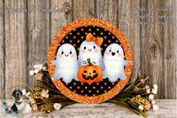 a Halloween-themed decoration with three ghostly figures and a jack-o-lantern, all set against a wooden background. The decoration is surrounded by a black and orange border, and there are flowers and greenery in the foreground.
