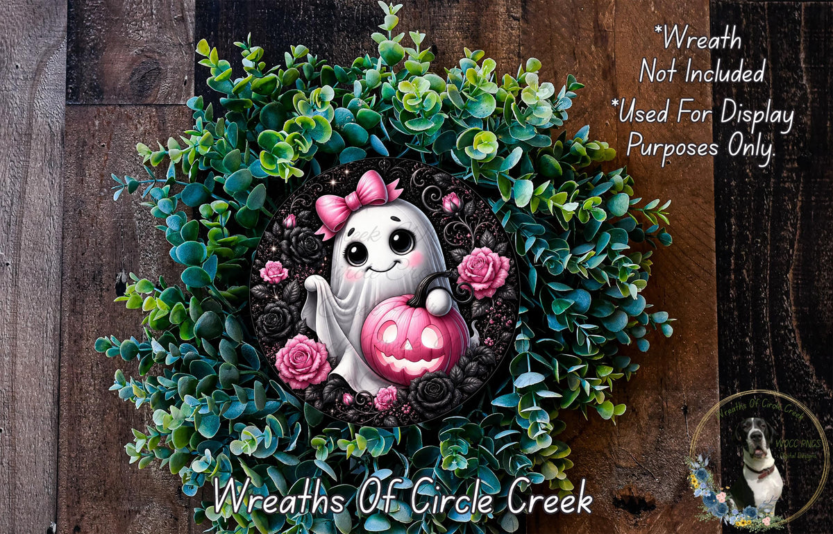 a Halloween-themed wreath with a ghost holding a pumpkin and a pink bow. The wreath is surrounded by green foliage and has a wooden background.