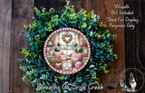 a wreath with a decorative plate containing a scene of a cozy indoor setting, including a window, a heart-shaped decoration, and various other decorative elements.