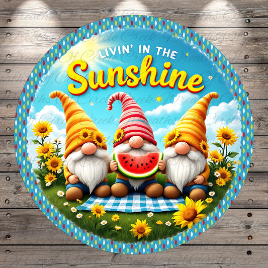 A round, colorful sign featuring three gnomes sitting on a grassy field with flowers and sunflowers, holding a watermelon slice. The sign has a cheerful, sunny atmosphere and includes the text "LIVIN' IN THE SUNSHINE".