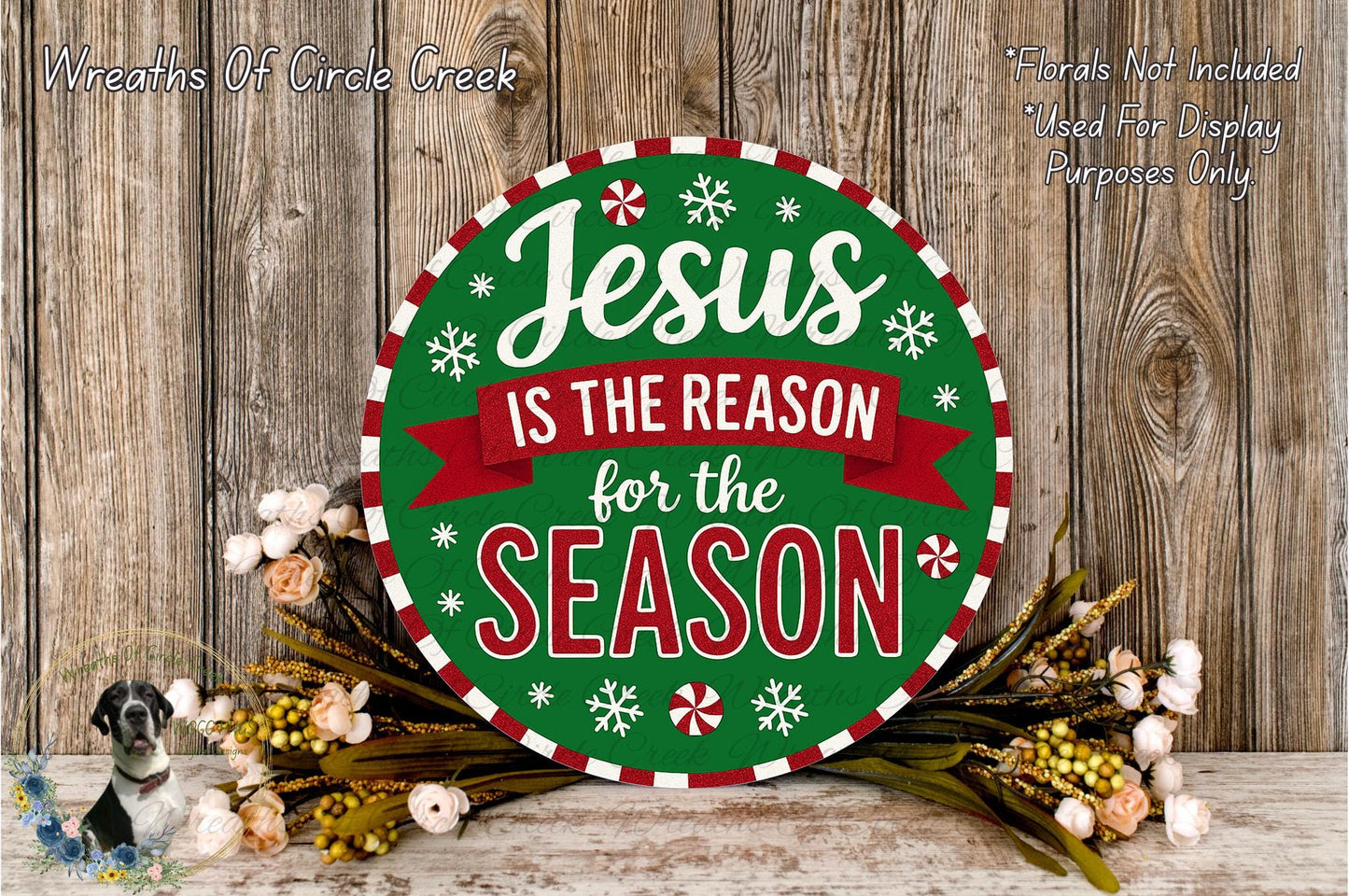 A circular sign with the text "Jesus is the reason for the season" surrounded by a wreath of flowers and greenery, placed on a wooden surface.