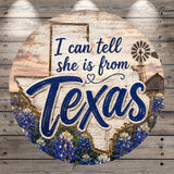 a circular sign with the text "I can tell she is from Texas" written on it. The sign is set against a background that includes a Texas state map, a windmill, and a field of blue flowers.