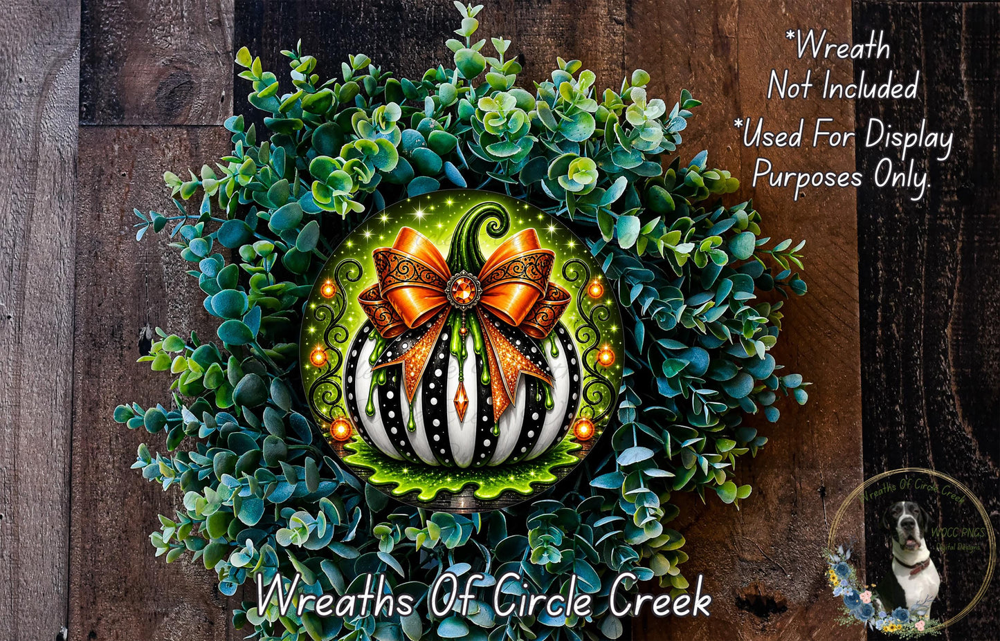 a wreath with a decorative pumpkin and a bow, surrounded by a lush green plant. The wreath is displayed on a wooden surface, and there is a small dog in the bottom right corner of the image.