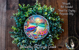 A colorful wreath made of green leaves and flowers, with a large circular design featuring a turtle, seashells, and a rainbow-colored background.