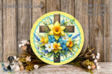 a decorative arrangement of a cross surrounded by a vibrant bouquet of yellow and blue flowers, placed on a wooden surface.