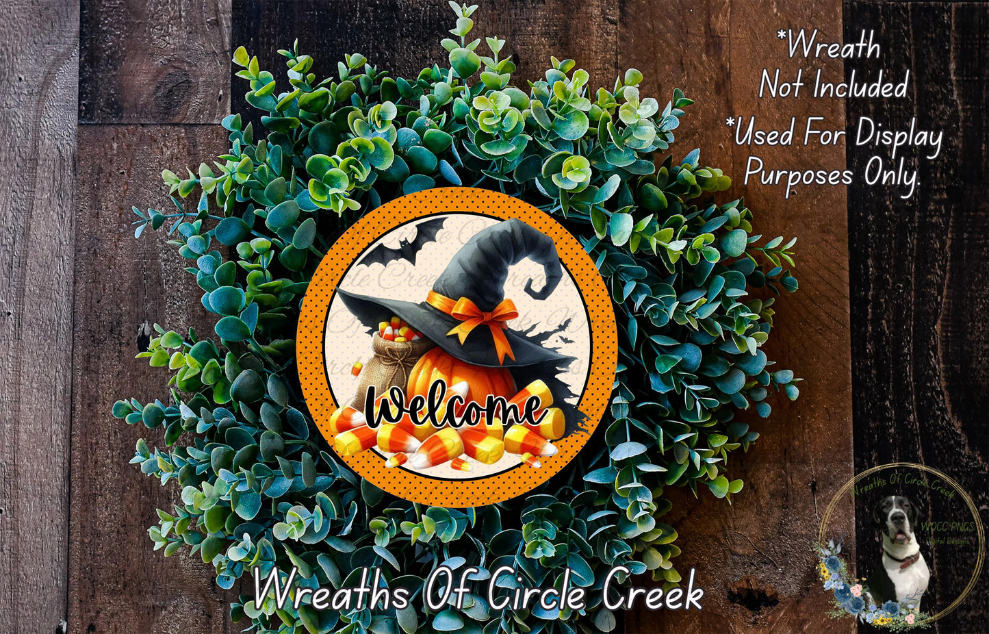 a Halloween-themed wreath with a witch's hat, a pumpkin, and candy corn, surrounded by greenery. The wreath is displayed on a wooden surface, and there is a text overlay that reads "Welcome Wreath Not Included * Used For Display Purposes Only".