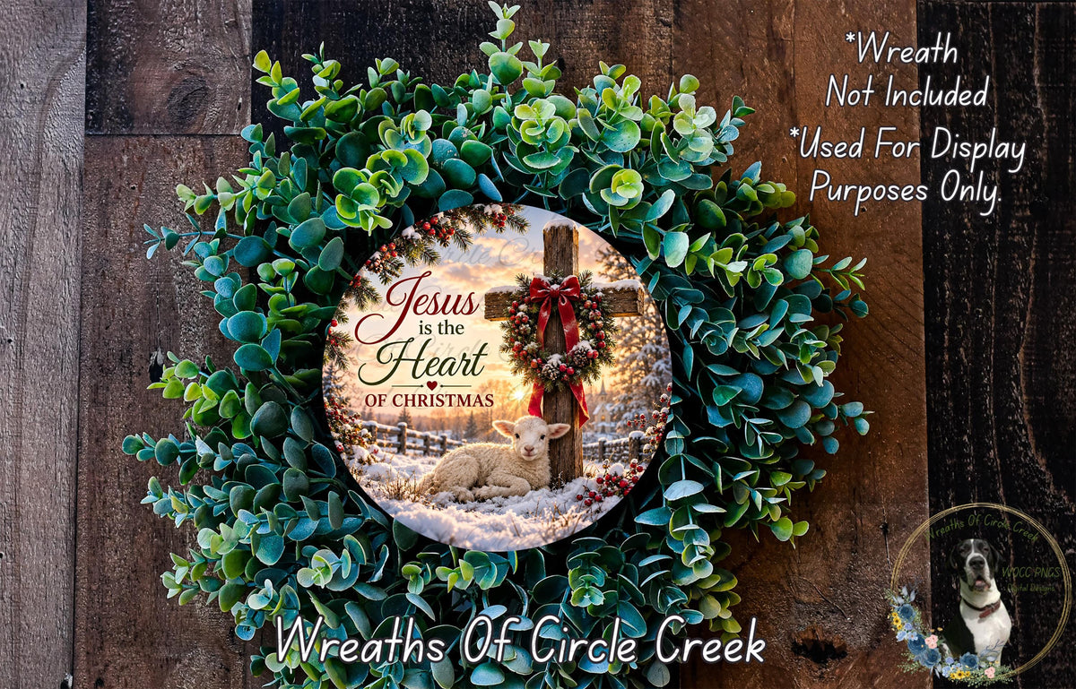 A wreath made of green leaves and a red ribbon, with a circular design featuring a lamb and a cross, hanging on a wooden wall.