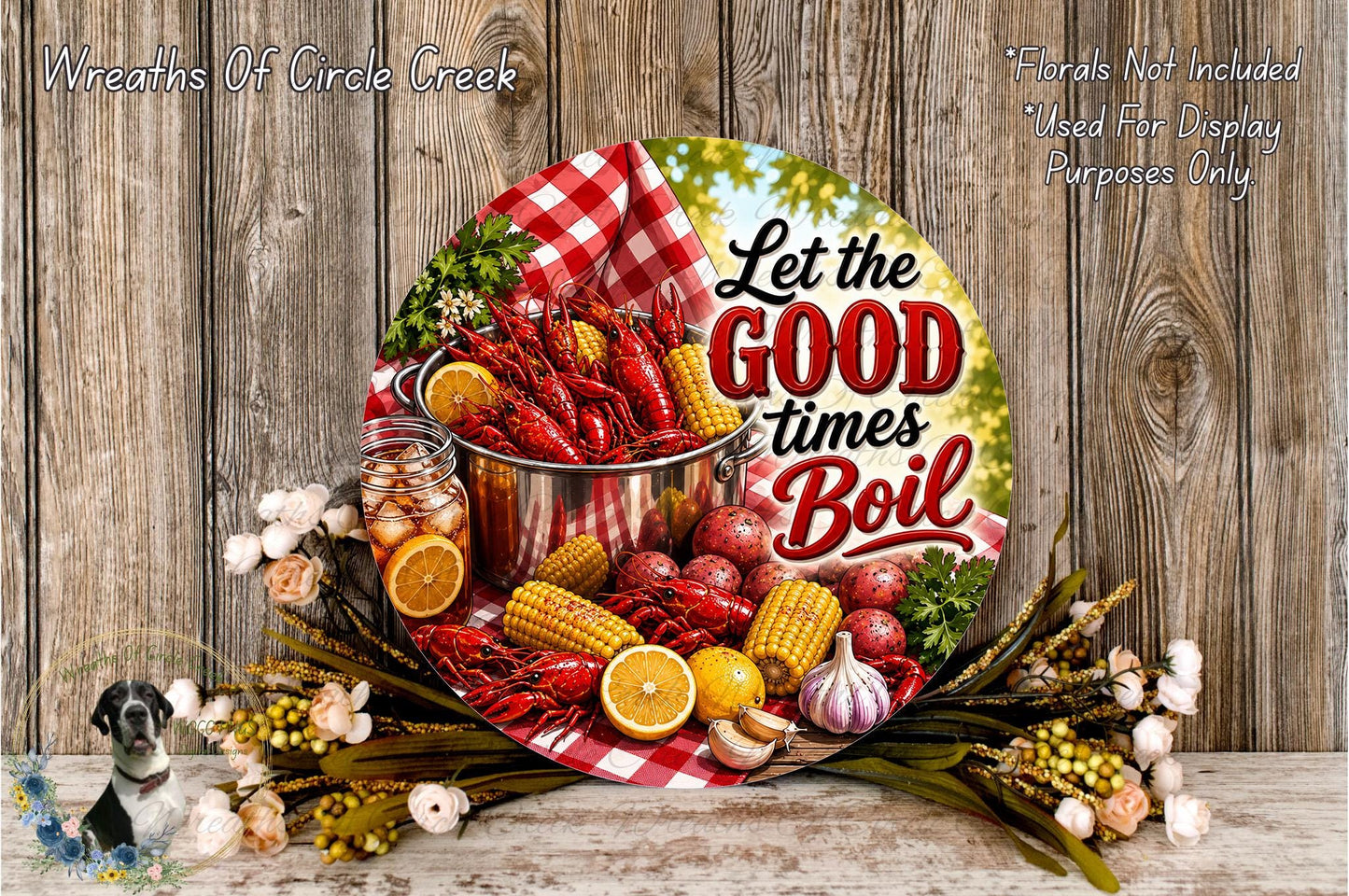 A decorative plate with a red and white checkered cloth, surrounded by various food items such as corn, oranges, and a pot of crawfish. The plate has a message that says "Let the good times boil".