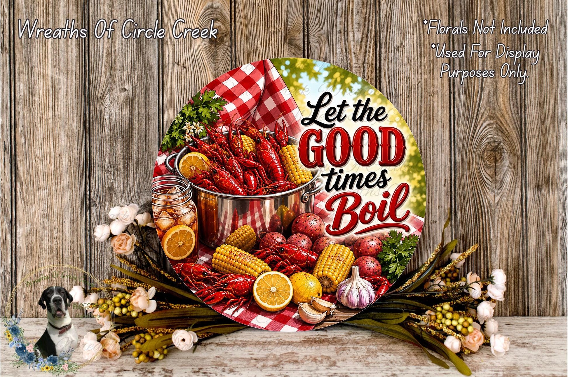 A decorative plate with a red and white checkered cloth, surrounded by various food items such as corn, oranges, and a pot of crawfish. The plate has a message that says "Let the good times boil".