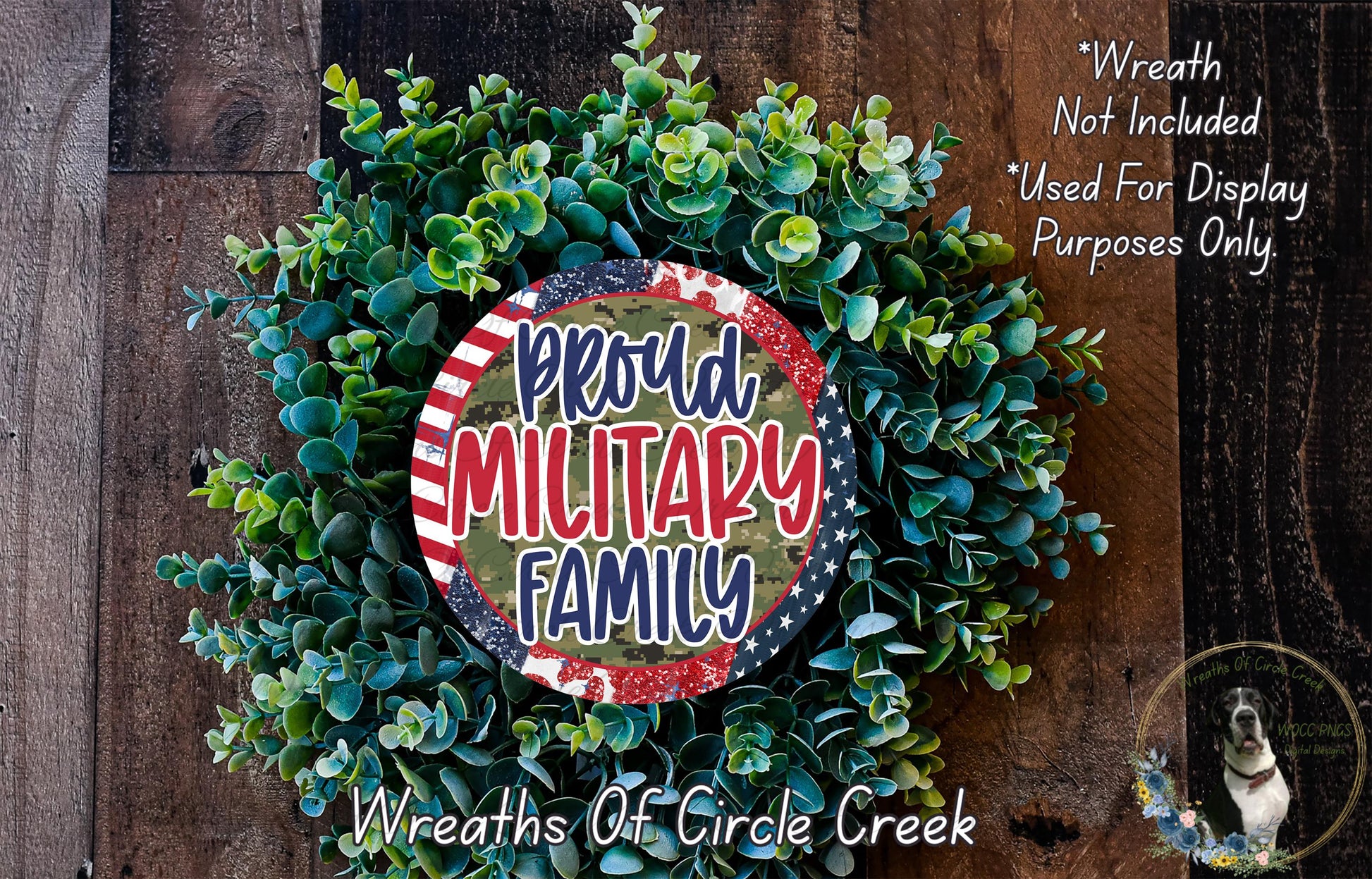 a wreath made of green leaves and a circular sign with the text "Proud Military Family" in the center. The wreath is displayed on a wooden surface, and there is a small dog in the bottom right corner of the image.