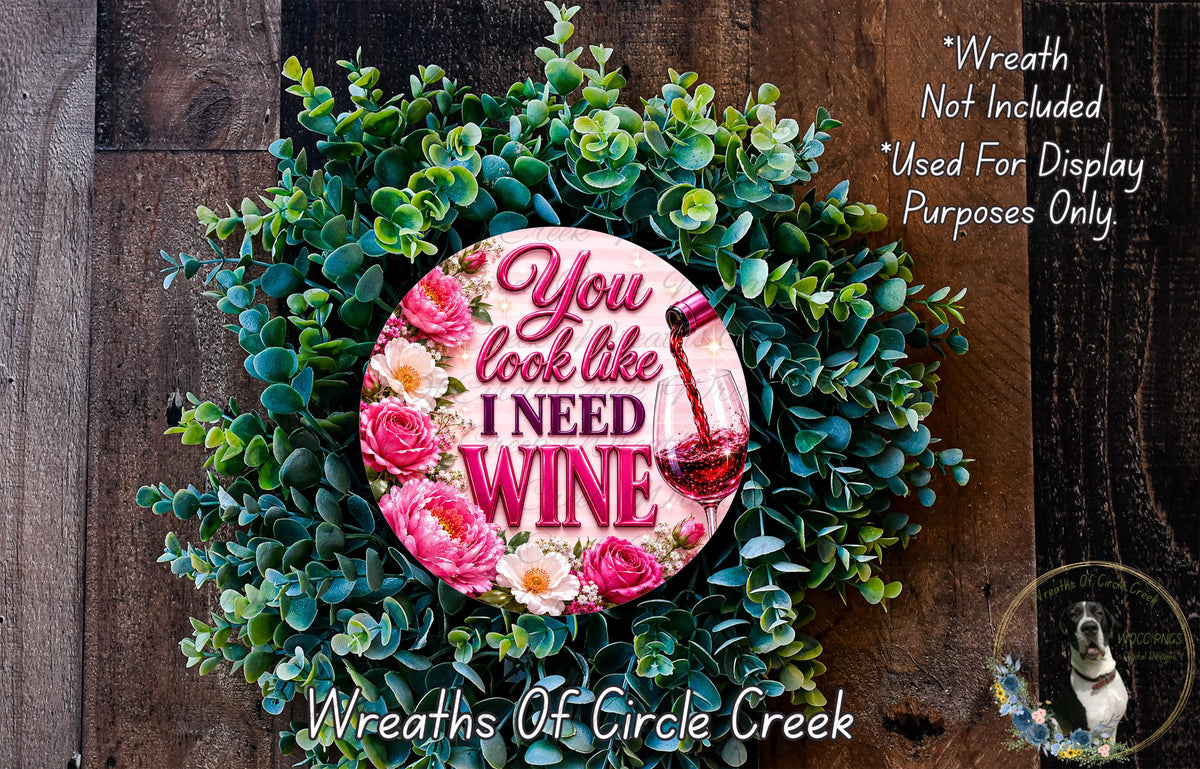 A wreath made of green leaves and pink flowers, with a pink sign that says "You look like I need wine".