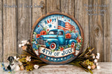 A circular wooden sign with a blue truck and American flag design, surrounded by flowers and greenery, against a wooden background.