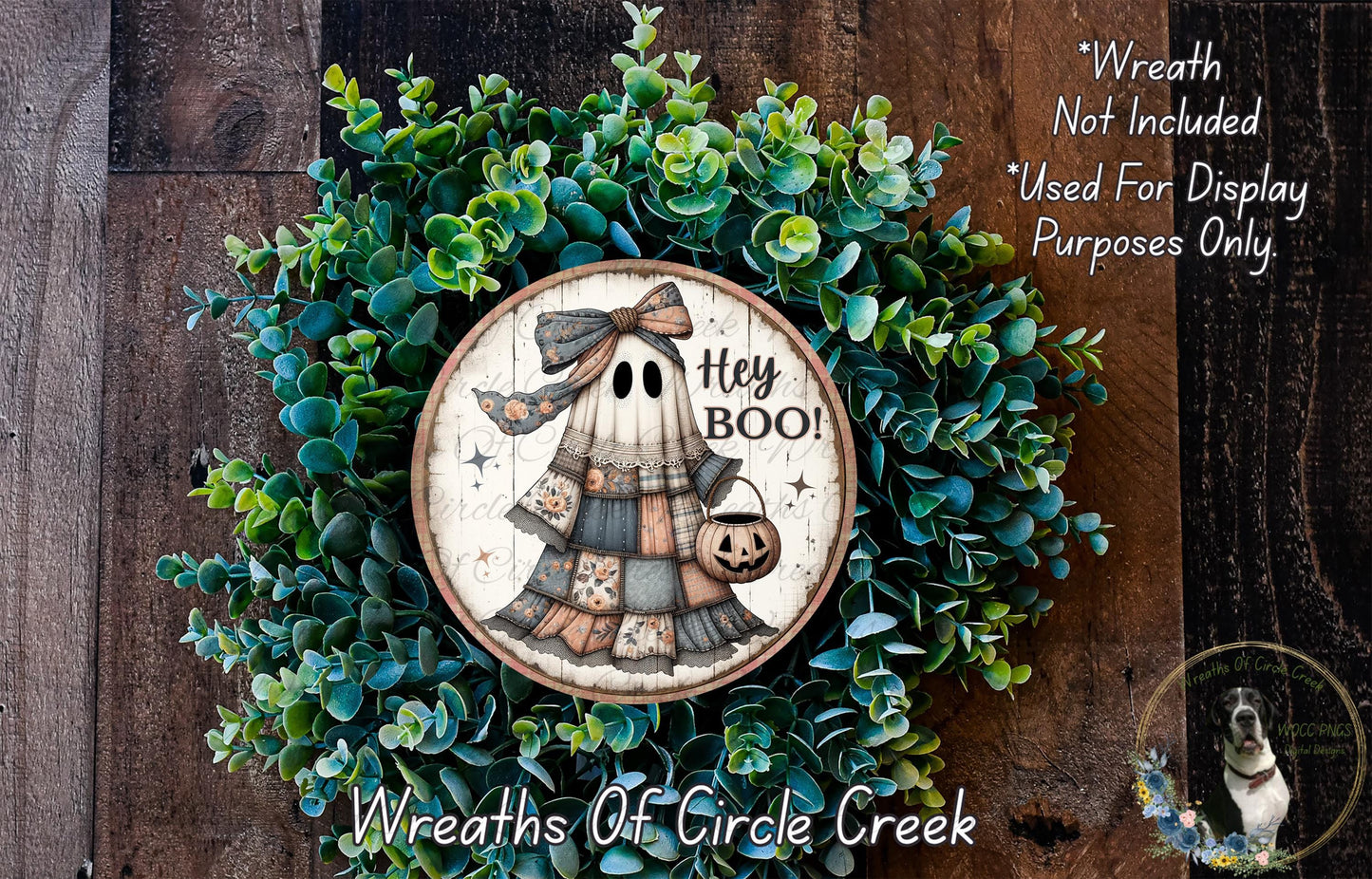 a Halloween-themed wreath with a ghost holding a "Hey Boo!" sign, surrounded by green foliage. The wreath is displayed on a wooden surface, and there is a small dog visible in the bottom right corner.