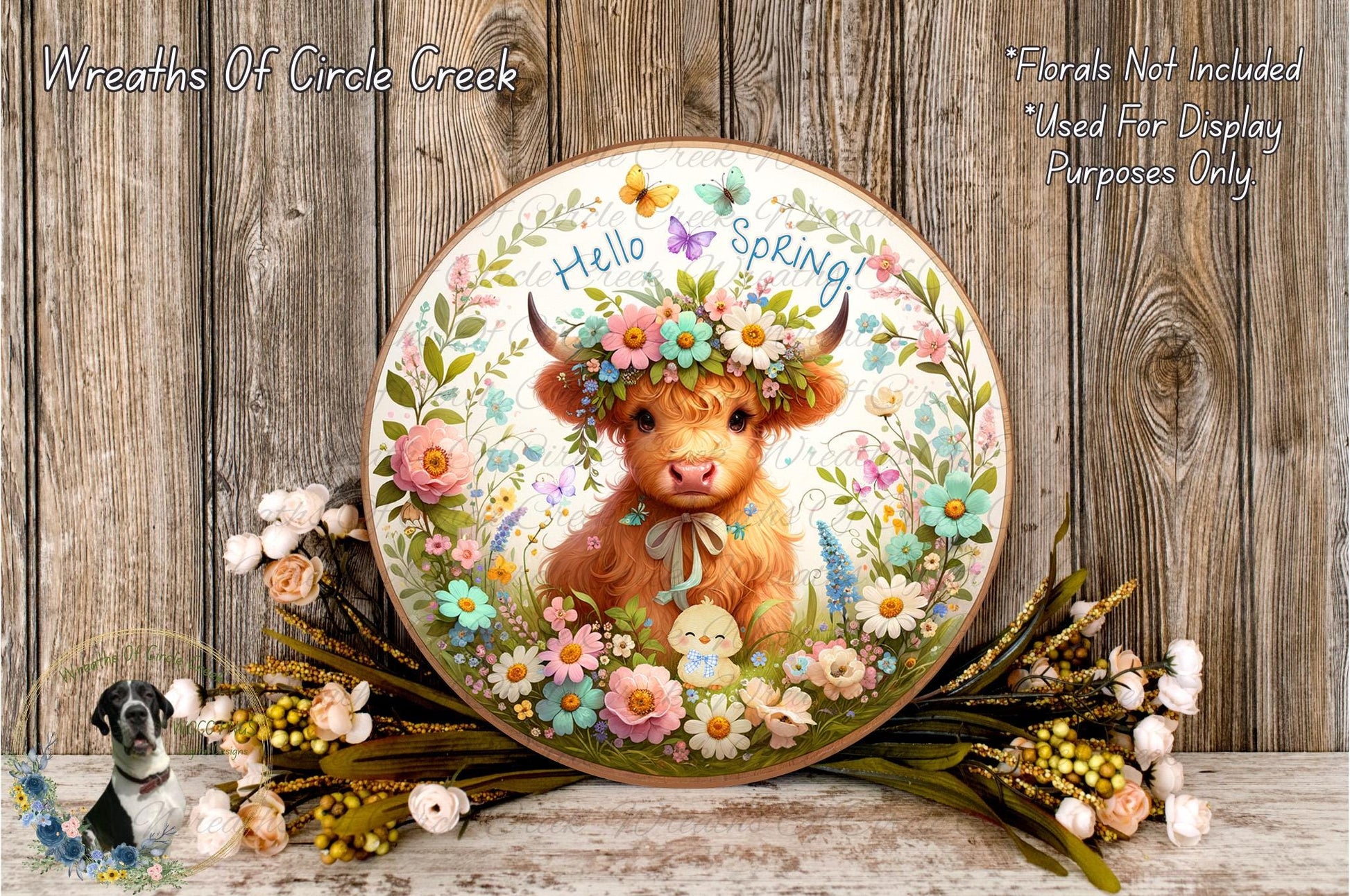A decorative plate featuring a cow surrounded by a floral arrangement, with the text "Hello Spring" on it. The plate is placed on a wooden surface, and there are flowers and greenery surrounding it.