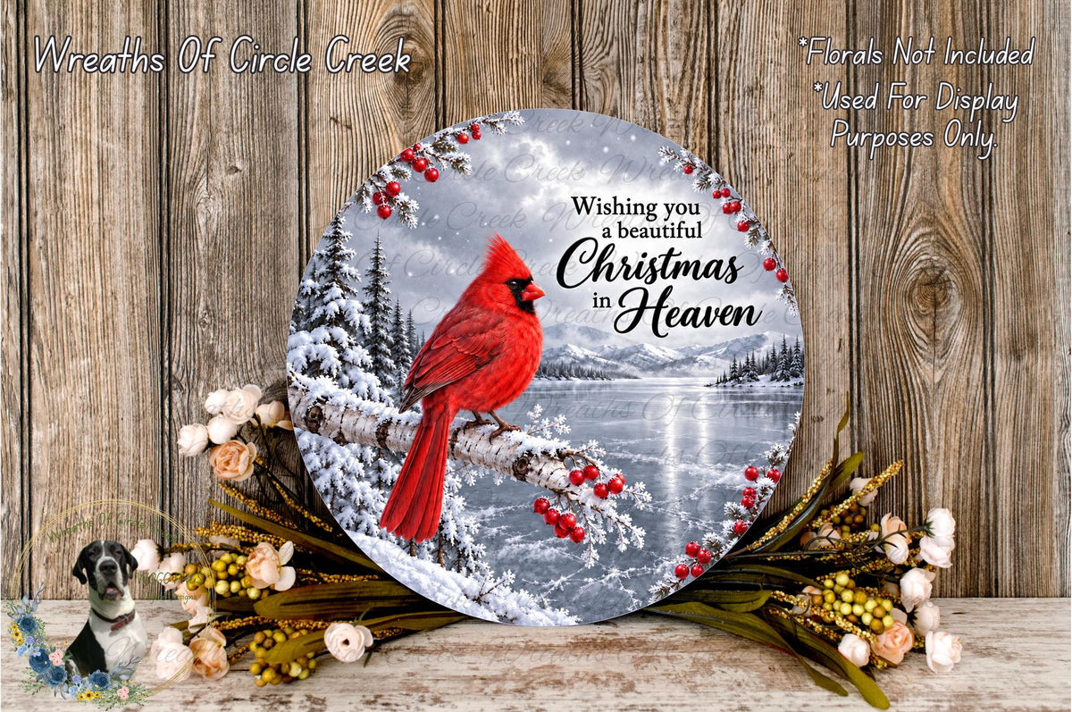 A round, wooden plaque with a red cardinal perched on a branch, surrounded by a wreath of flowers and a snowy landscape. The plaque features a message wishing a beautiful Christmas in Heaven.