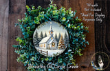 A wreath with a winter scene of a church and pine trees, featuring a star in the sky, is displayed on a wooden background.