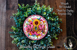 A wreath made of various green plants and flowers, with the word "MOM" prominently displayed in the center.