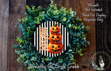 a Halloween-themed wreath made of green foliage and three jack-o'-lanterns. The wreath is displayed on a wooden surface, and there is a text overlay that reads "Wreath Not Included * Used For Display Purposes Only".