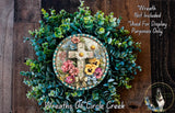 a wreath with a cross and flowers, surrounded by a lush green plant. The wreath is displayed on a wooden surface, and there is a small dog in the bottom right corner of the image.