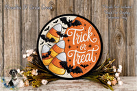 a Halloween-themed sign with the text "Trick or Treat" and illustrations of candy corn and bats. The sign is displayed on a wooden surface, surrounded by a floral arrangement and some flowers.
