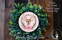 A wreath made of green leaves and a pink bow with a deer head in the center, placed on a wooden surface.