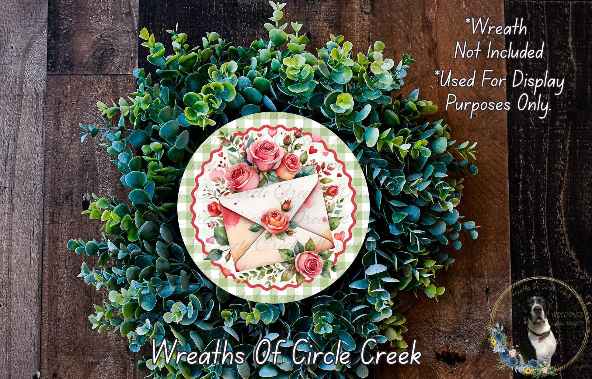 a wreath made of green leaves and roses, with a white envelope and red roses on it. The wreath is displayed on a wooden surface, and there is a small dog in the bottom right corner of the image.