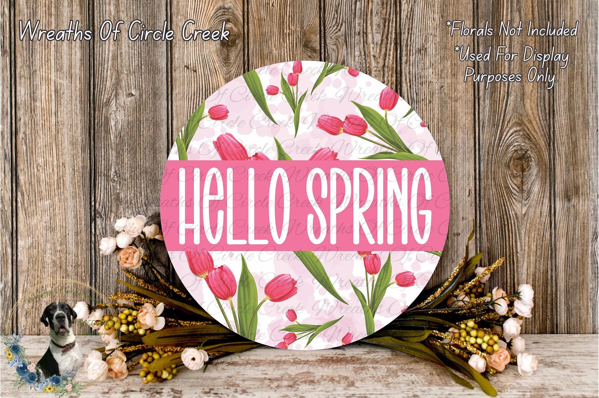 a round sign with the text "Hello Spring" surrounded by a floral arrangement of pink tulips and greenery.