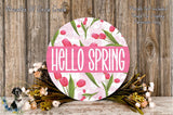 a round sign with the text "Hello Spring" surrounded by a floral arrangement of pink tulips and greenery.