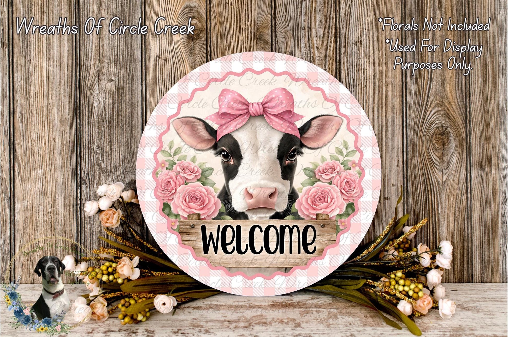 a decorative sign with a cow's face and pink flowers, surrounded by a floral arrangement and a wooden background.