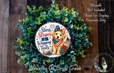 a wreath made of green leaves and a dog wearing a patriotic American flag. The wreath is displayed on a wooden surface, and there is a small dog visible in the background.