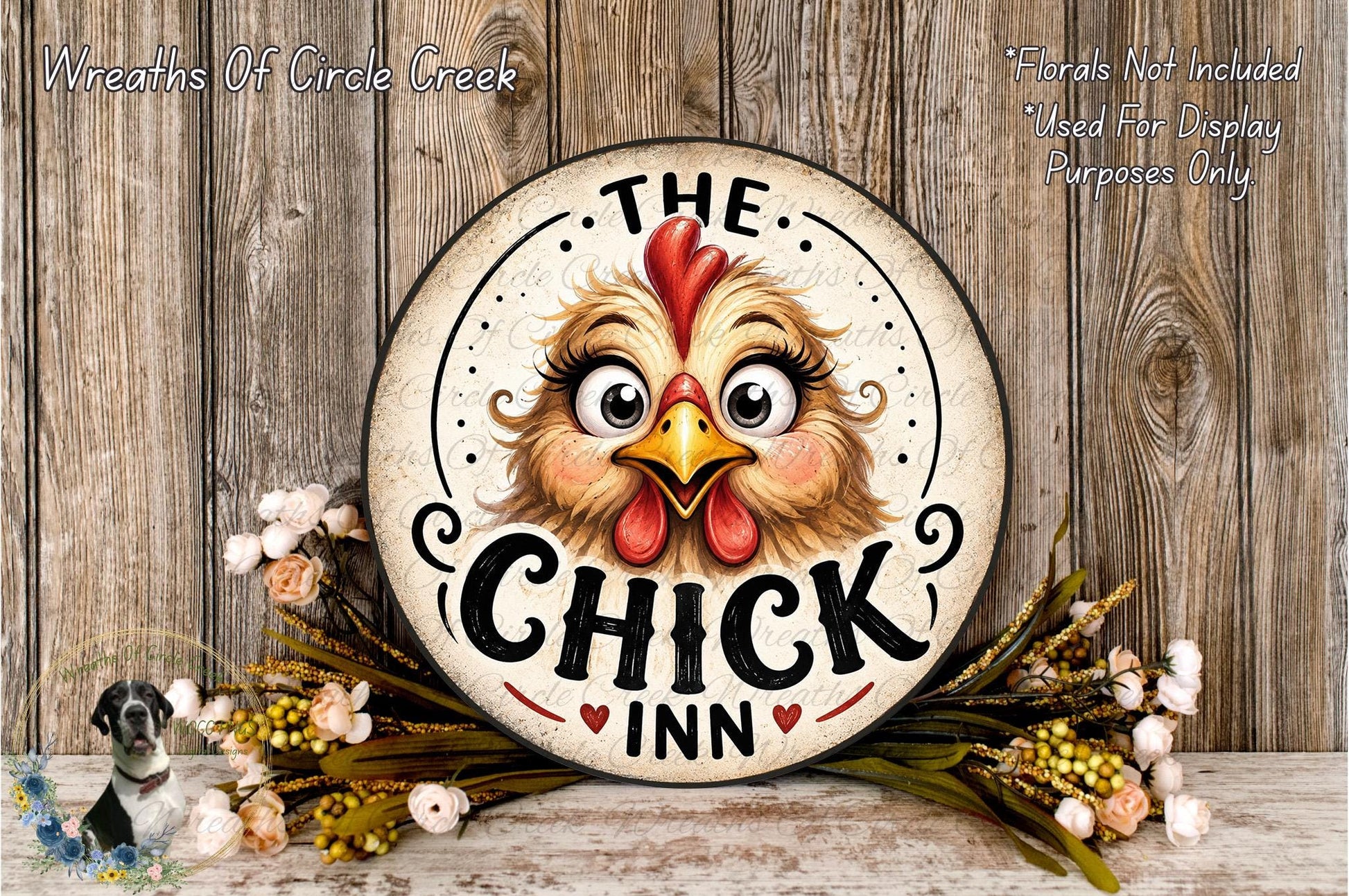 a decorative sign with a cartoon chicken face, surrounded by flowers and placed on a wooden surface.