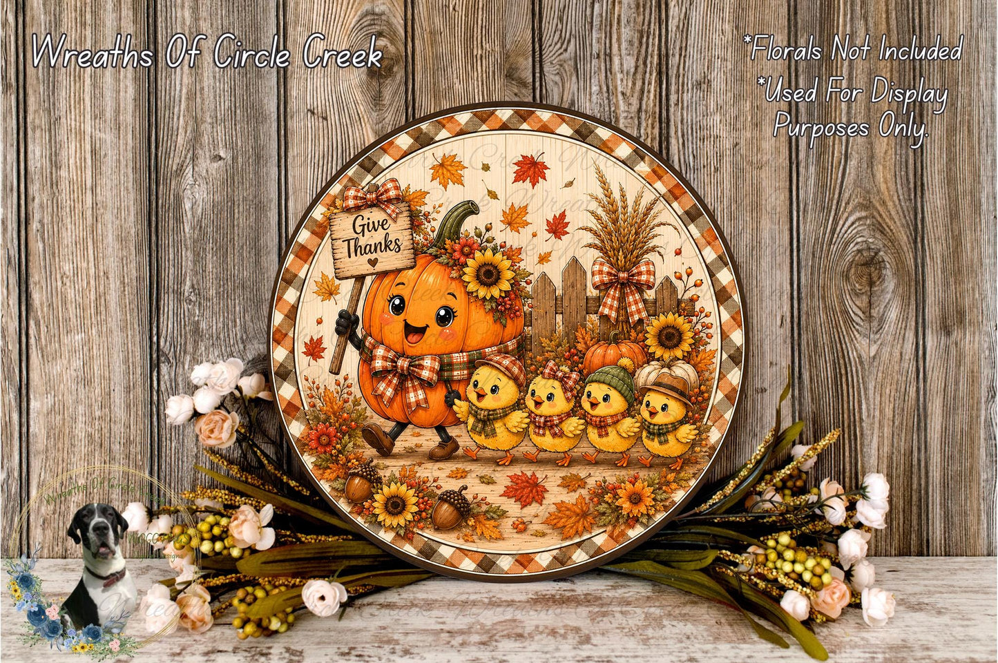 A decorative plate featuring a pumpkin character surrounded by small yellow chicks, with a sign that says "Give Thanks". The plate is placed on a wooden surface, and there are flowers and leaves surrounding it.
