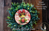 a wreath with a frog wearing glasses and a bow, surrounded by greenery. The wreath is displayed on a wooden surface, and there is a text overlay that reads "Happy Valentine's Day" and "Wreaths of Circle Creek".