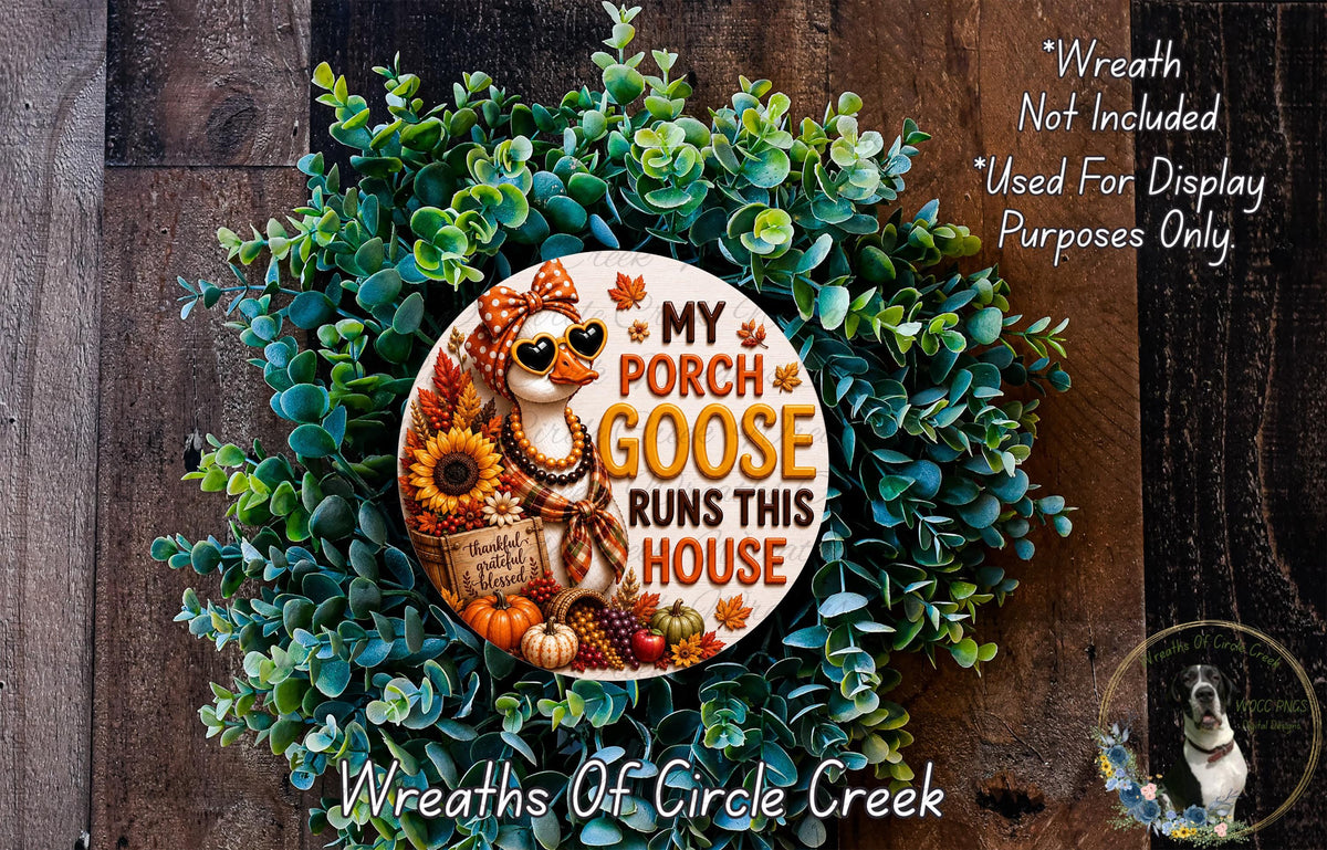 a wreath made of various fall-themed elements, including a goose, sunflowers, pumpkins, and a sign that says "My Porch Goose Runs This House". The wreath is displayed on a wooden surface, and there is a small dog in the bottom right corner of the image.