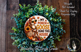 a wreath made of various fall-themed elements, including a goose, sunflowers, pumpkins, and a sign that says "My Porch Goose Runs This House". The wreath is displayed on a wooden surface, and there is a small dog in the bottom right corner of the image.