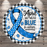 A blue ribbon with the text "in April we wear blue for autism awareness" is displayed against a wooden background with a checkered pattern.