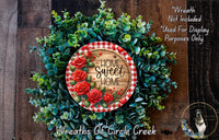 a wreath made of green foliage and red roses, with a wooden sign that reads "Home Sweet Home" in the center.