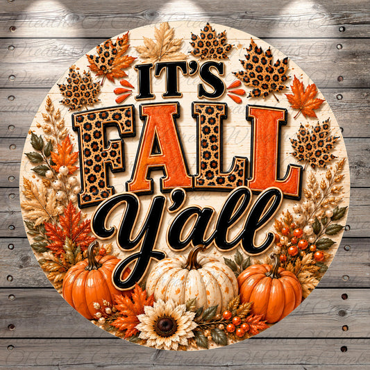 A decorative circular sign with the text "It's Fall Y'all" surrounded by autumn-themed elements such as leopard print leaves, pumpkins, and sunflowers.