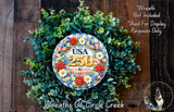 A wreath made of green leaves and flowers, with a circular sign displaying the text "USA 250" surrounded by red roses and white daisies.