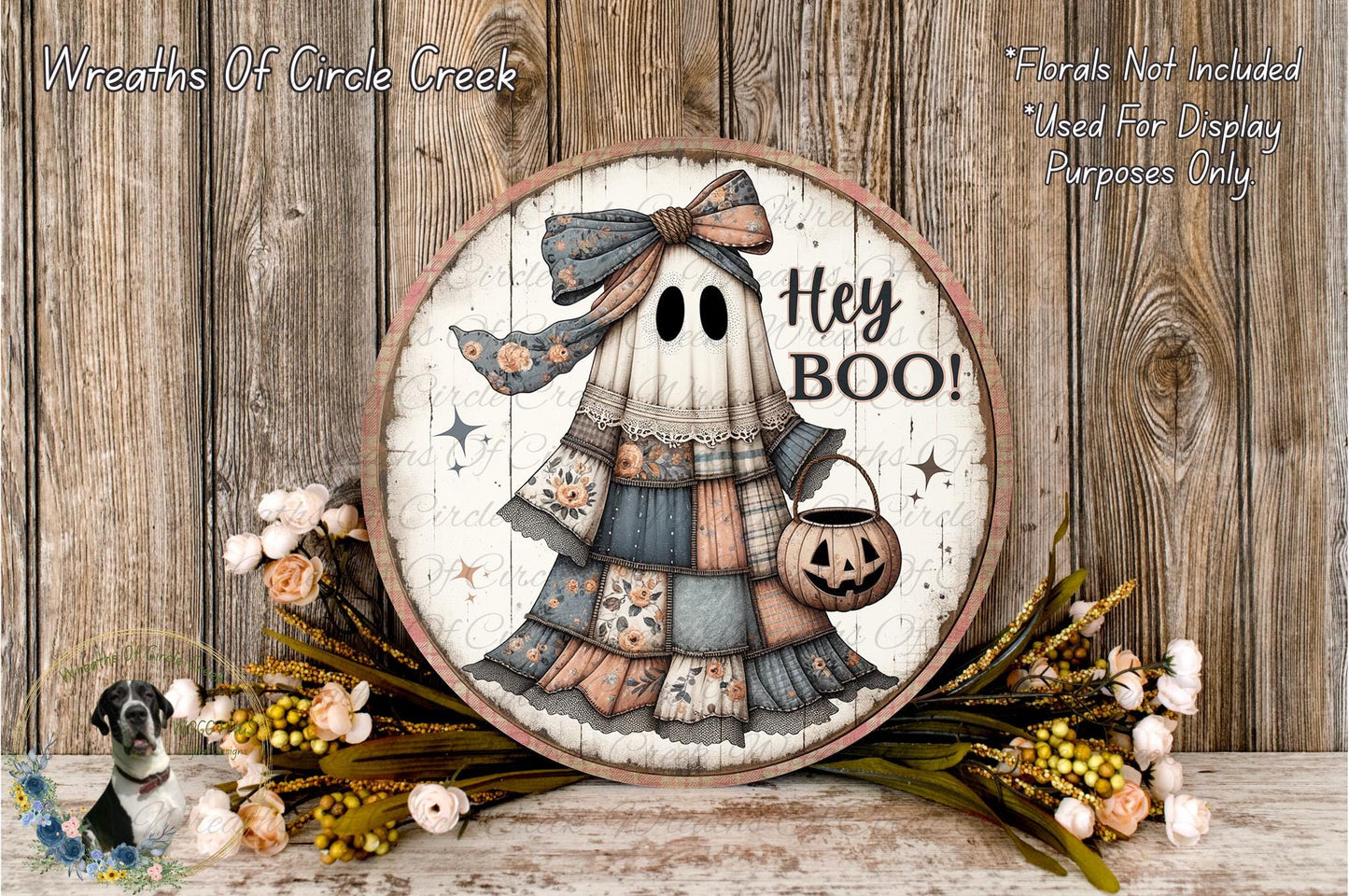 a Halloween-themed decoration with a ghost wearing a dress and holding a pumpkin. The ghost has a bow on its head and the text "Hey Boo!" written on it. The decoration is displayed on a wooden surface, surrounded by flowers and greenery.