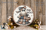 a Halloween-themed decoration with a ghost wearing a dress and holding a pumpkin. The ghost has a bow on its head and the text "Hey Boo!" written on it. The decoration is displayed on a wooden surface, surrounded by flowers and greenery.