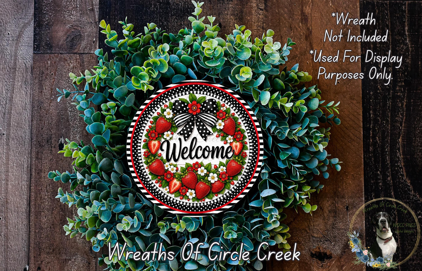 a wreath made of green leaves and red berries, with a white and black border, and a "Welcome" sign in the center. The wreath is displayed on a wooden surface, and there is a small dog in the bottom right corner.