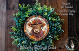 a wreath with a cow's head on it, surrounded by green leaves and flowers. The wreath is displayed on a wooden surface, and there is a small dog in the bottom right corner of the image.
