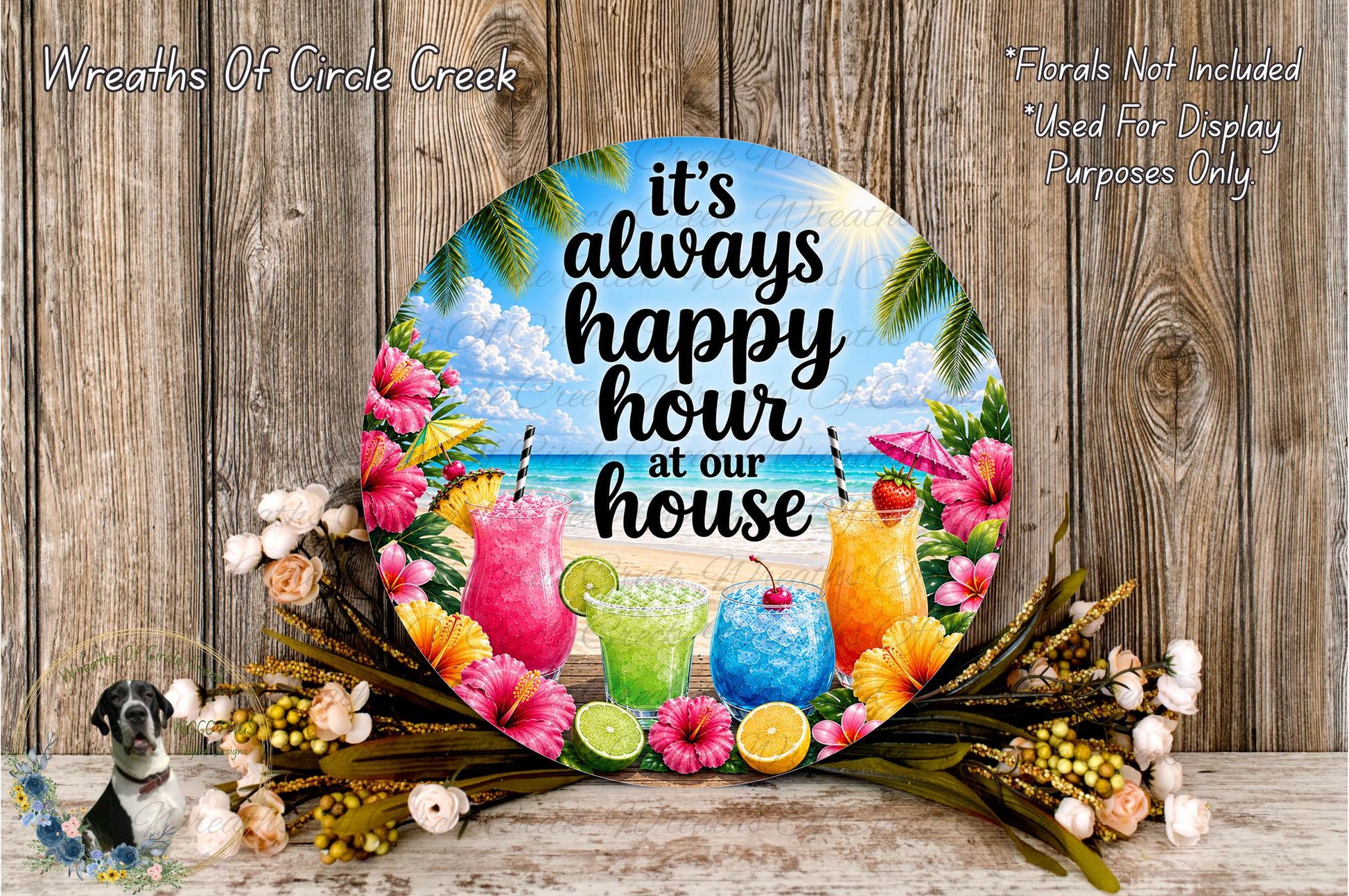 a round sign with a tropical beach theme, surrounded by colorful flowers and tropical drinks. The sign reads "It's always happy hour at our house" and is displayed on a wooden surface.