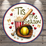 A round decorative plate with a baseball theme, featuring a baseball bat, popcorn, a softball, a glove, and hearts. The plate has the text "Tis the Season" written on it.