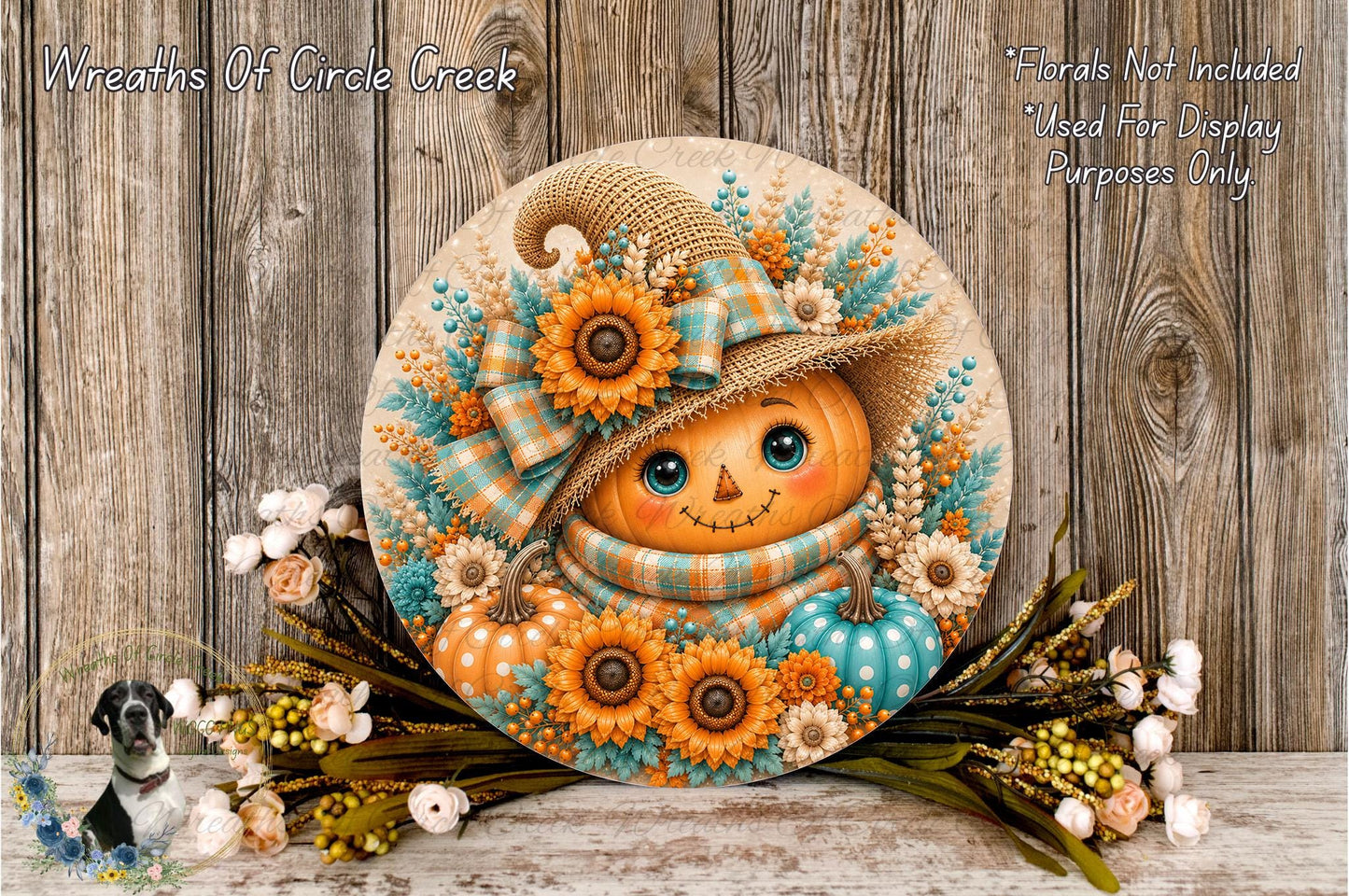 A decorative wreath featuring a pumpkin face with a hat and floral elements, placed on a wooden surface with a sprig of flowers and greenery.